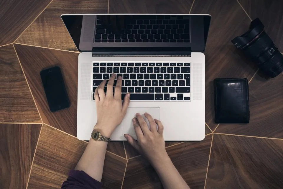 Person typing on a laptop at a wooden desk